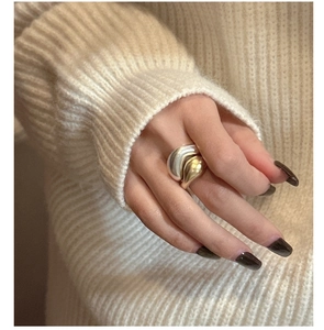 Detail of two-tone gold and silver wavy ring on hand with beige knit background