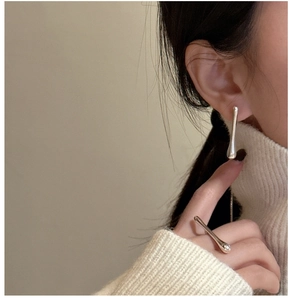 Detail of silver liquid flow ring and teardrop earrings on model in white sweater
