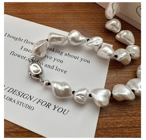 Detail of baroque pearl necklace with knotted black cord and silver clasp on wood
