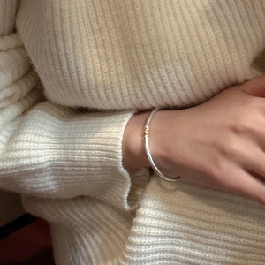 Bracelet jonc ouvert bicolore en argent S925 avec perle dorée sur un poignet féminin