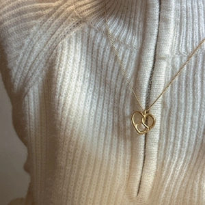 Collier minimaliste en forme de cœur doré porté par un mannequin en pull beige