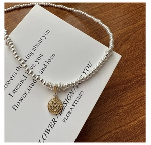 Macro shot of silver beaded chain with a vintage gold coin pendant and sparkling zircon stone