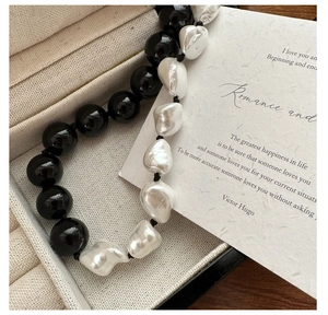 Macro shot of s925 silver necklace with black agate and baroque pearls on beige tray