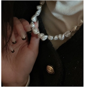 Detail of baroque pearl necklace worn on neck with elegant tweed jacket and white top