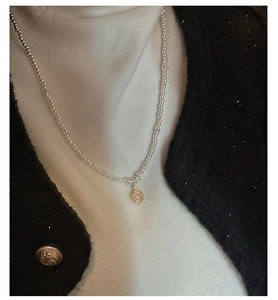 Detail of S925 silver beaded necklace featuring a vintage gold coin pendant on a tweed jacket