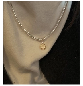Detail of silver bead chain with gold vintage coin pendant worn on a white turtleneck