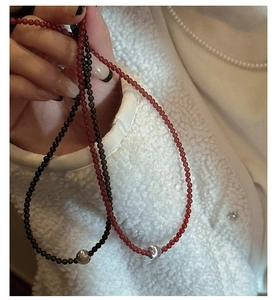 Detail of beaded s925 silver necklaces with black and red beads on soft white fabric