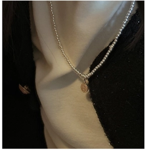 Macro shot of silver beaded chain with a vintage coin pendant featuring heart and laurel