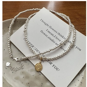 Detailed macro of S925 sterling silver beaded necklace with golden coin pendant and lobster clasp