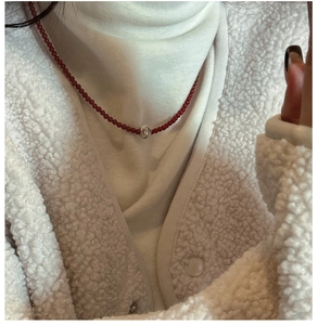 Detail shot of a red beaded necklace with a central silver bead on a model wearing white
