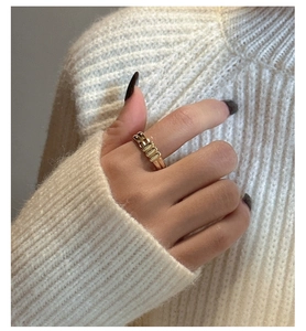 Detailed view of a gold geometric ring on a finger against a beige knit sweater