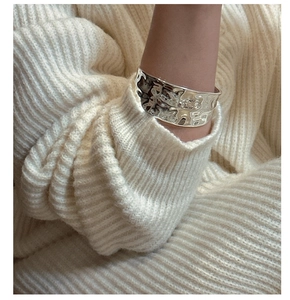 Detail of wide hammered S925 sterling silver cuff bracelet on white knit sweater
