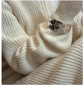 Close-up of a wide silver cuff bracelet with hammered texture on a white knit sweater