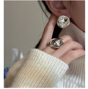 Close-up of a silver liquid metal ring and spherical earrings set on a knit sweater