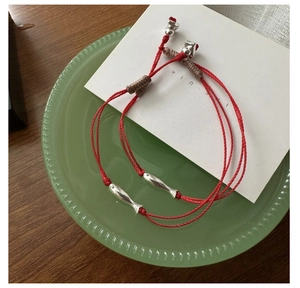 Détail macro de bracelets tissés rouges avec pendentifs poissons en argent sur une assiette