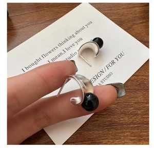 Detailed view of C-shaped matte silver earrings with black onyx bead on a person's hand