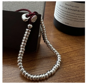 Gros plan de perles en argent sterling S925 et cordon tressé rouge sur fond de bois naturel