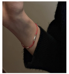 Gros plan d'un bracelet en corde tressée rouge avec un tube en argent porté au poignet