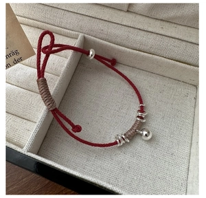 Dettaglio del bracciale cordino rosso intrecciato con sfere d'argento e campanellino