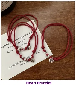 Close-up of three handmade red cord bracelets with silver heart charms on a wooden table