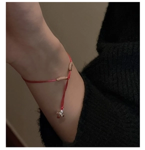 Détail du bracelet en soie tressée rouge avec accents dorés et breloque en argent