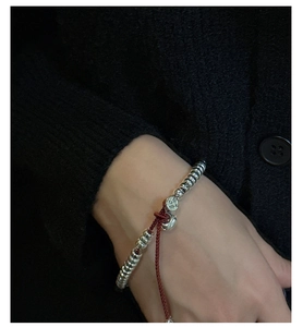 Détail du bracelet perlé en argent S925 avec cordon rouge et pendentif rond gravé