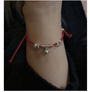 Dettaglio del bracciale rosso fatto a mano con ciondolo campanello argento al polso