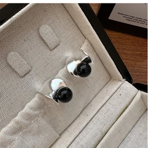 Macro shot of minimalist S925 silver earrings with black onyx on a beige fabric lining