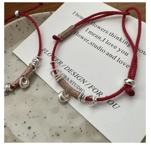 Detail of S925 silver sycee charms on red braided rope bracelets with silk wrap knots