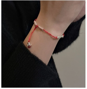 Gros plan d'un bracelet tressé rouge avec pendentif poisson en argent sur le poignet
