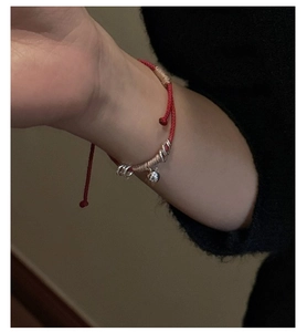 Dettaglio del bracciale di corda intrecciata rossa con anelli d'argento e campanellino