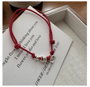 Detailed shot of red woven bracelet with silver heart charm and adjustable knots