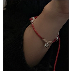 Close-up of a red woven rope bracelet with silver rings and beige thread on a wrist