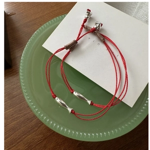 Détail du bracelet tressé rouge avec breloque poisson en argent sterling et nœuds réglables