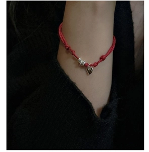 Macro shot of minimalist red rope bracelet with silver heart charm on black knit