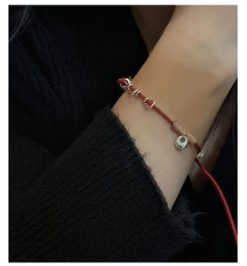 Detailed view of hand-woven red cord bracelet with silver ingots and charms on wrist