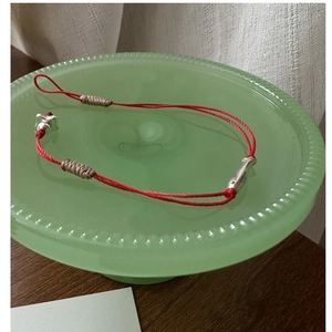 Détail d'un bracelet tressé rouge avec pendentifs poissons argentés sur plateau