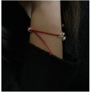 Bracciale intrecciato rosso minimalista con perline d'argento indossato su polso nero
