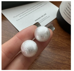 Detailed view of silver S925 earrings with brushed finish held between fingers