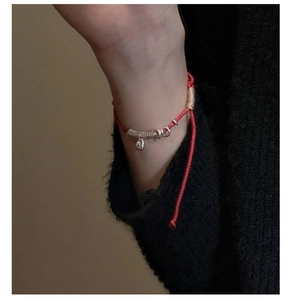 Detail of red braided cord bracelet with silver charms and water drop pendant on wrist