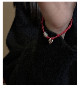 Detail view of red braided rope bracelet with S925 silver heart charm on model wrist
