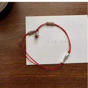 Détail d'un bracelet en corde rouge avec pendentif poisson en argent sur bois