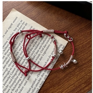Dettaglio di braccialetti in corda rossa intrecciata con perle e campanelli d'argento