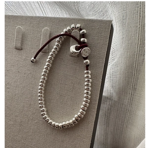 Détail des perles en argent S925 sur bracelet tressé rouge avec breloque de marque