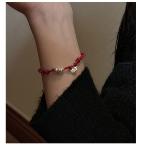 Detail of a red braided rope bracelet with a silver heart charm on a wrist
