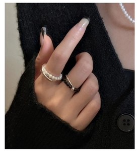 Detail of layered S925 sterling silver ring set with white pearls and brown beads on hand