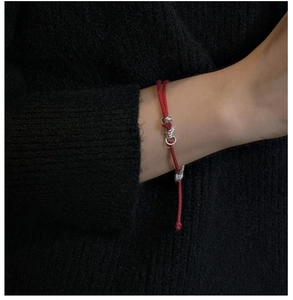 Detail of red braided cord bracelet with silver beads on wrist over black sweater