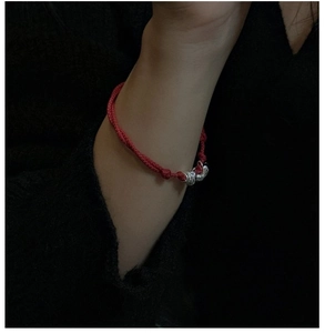 Close-up of red braided rope bracelet with silver rings on wrist against dark background