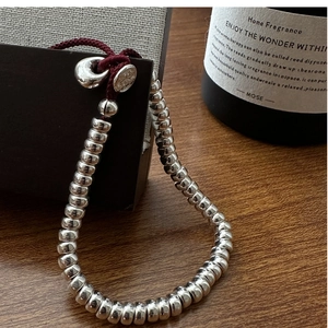 Détail du bracelet en perles d'argent S925 avec cordon bordeaux sur table en bois