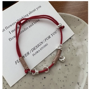 Detail of red braided silver bracelet with circular beads and teardrop pendant on ceramic plate